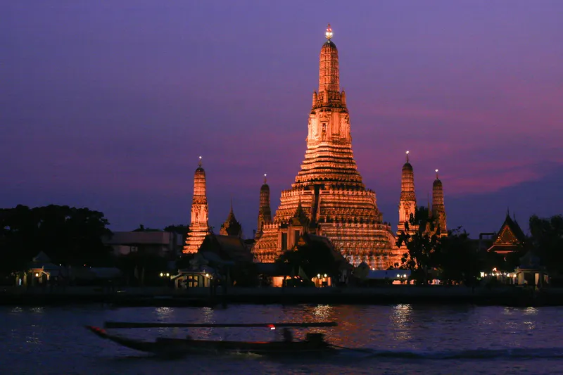 Wat Arun illuminated at blue hour across the Chao Phraya River