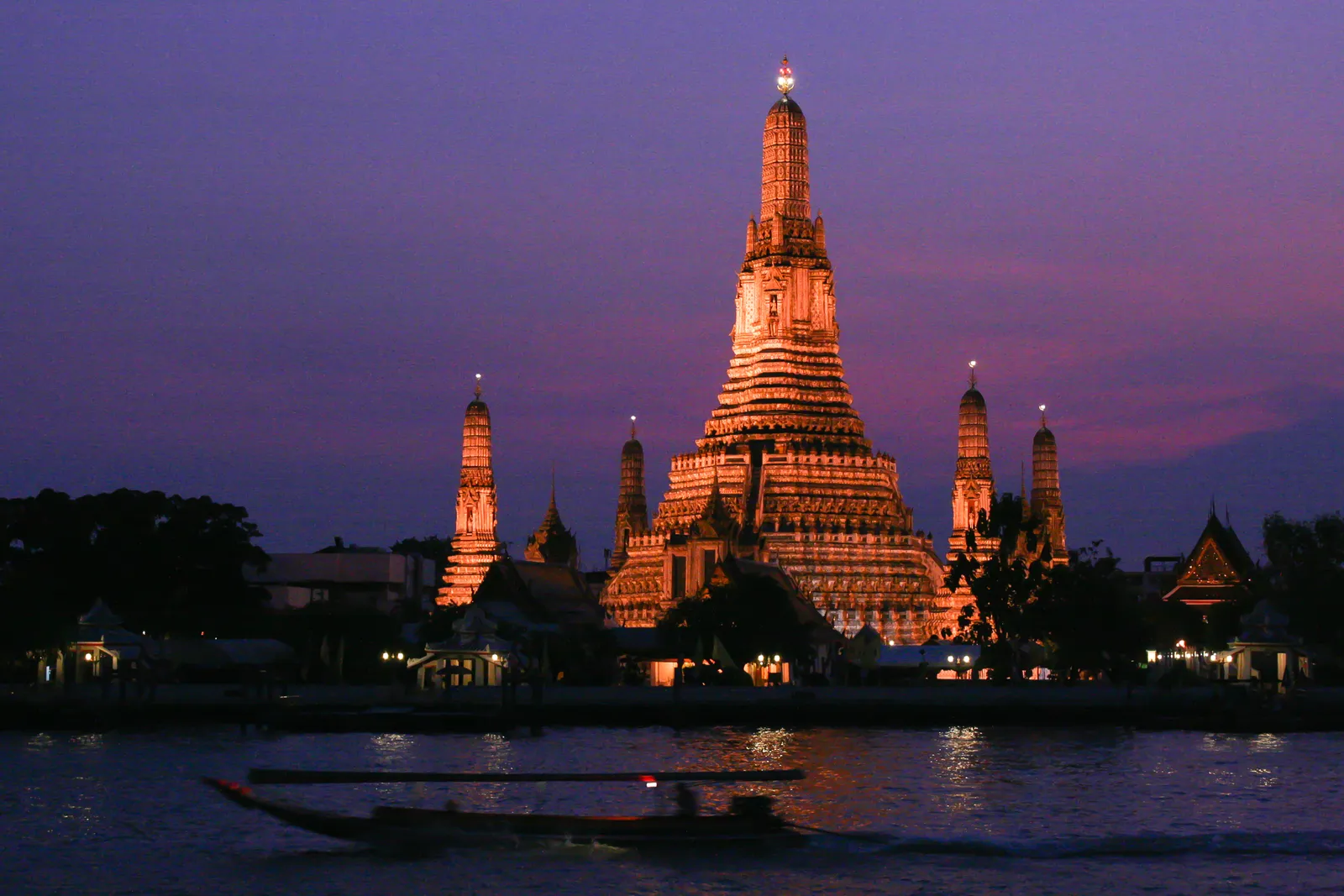 Wat Arun illuminated at blue hour across the Chao Phraya River